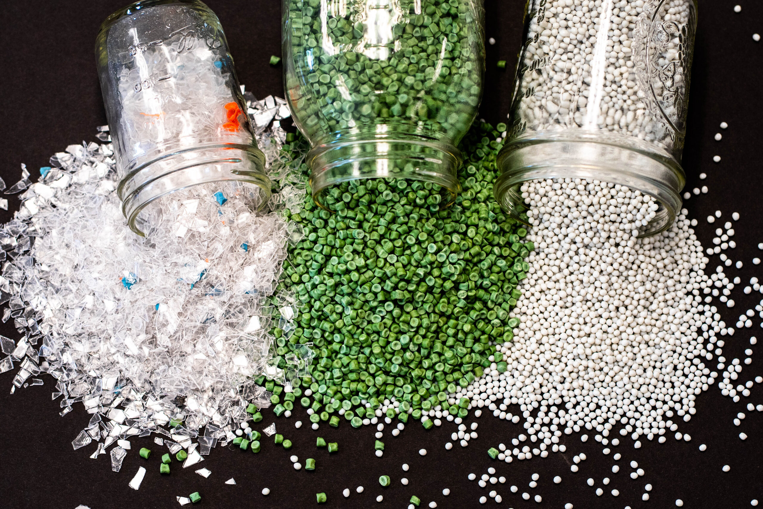 Jars of plastic regrind and resin pellets spilled on a dark surface
