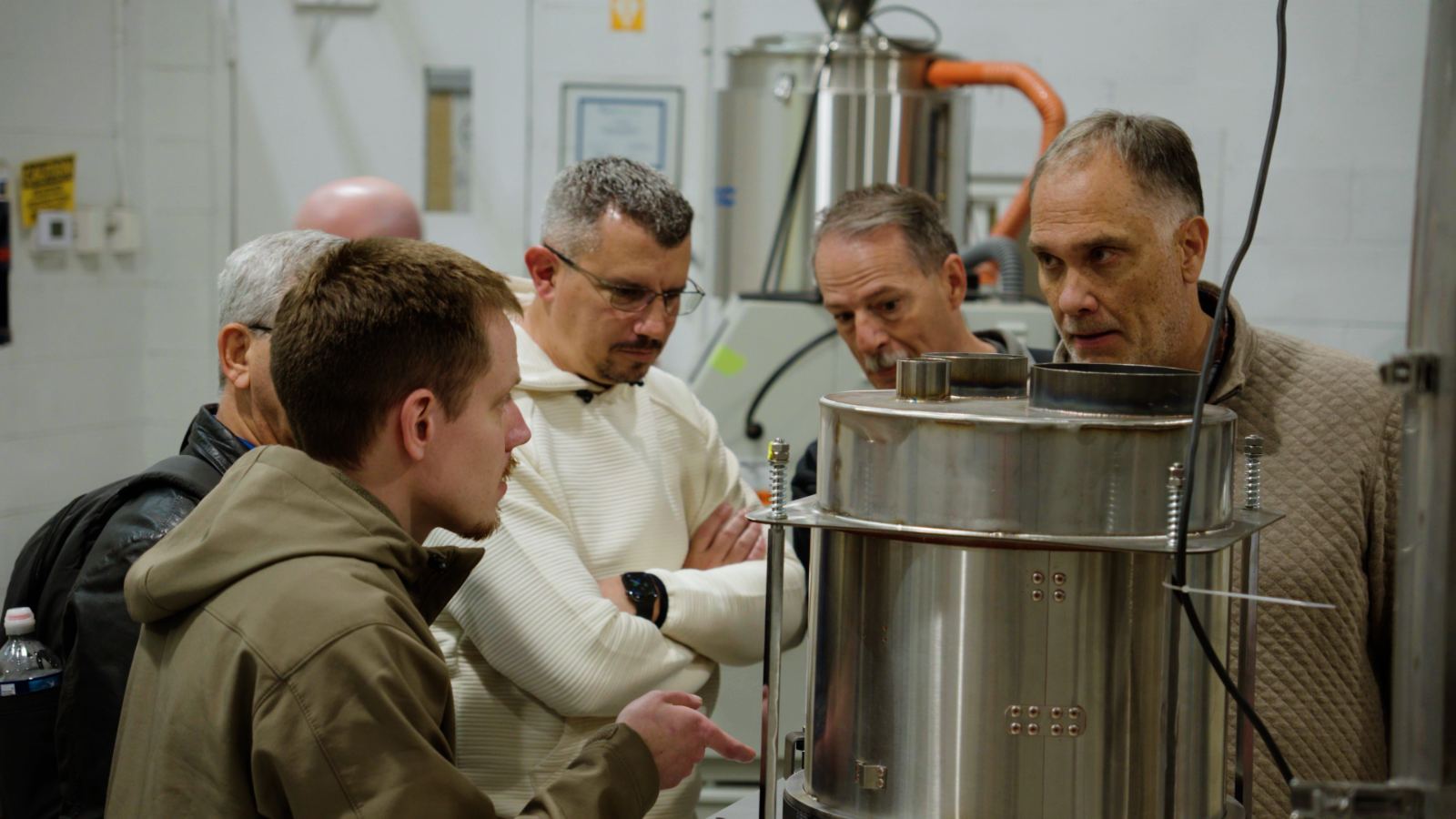 Processors and engineers examine a resin dryer alongside a Novatec lab technician